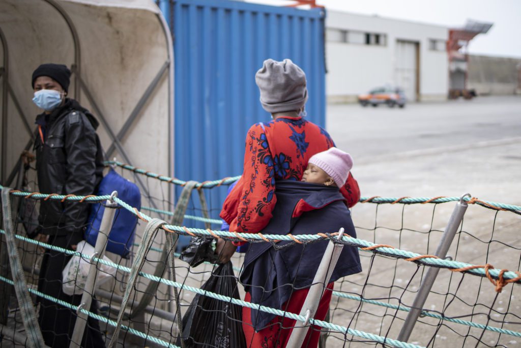 Zwei Frauen verlassen über den Gangway bei der Anlandung das Schiff. Eine Frau hat ein Baby in einer Trage auf ihrem Rücken.